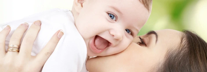 A mother holding her baby and kissing its cheek while the baby laughs