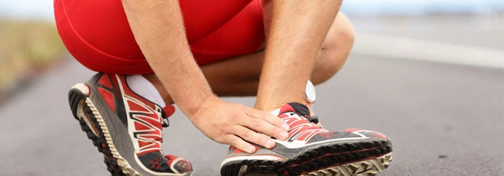 A runner with ankle pain holding their foot and ankle to stabilize it