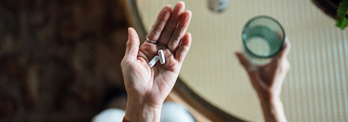A person holding medication in one hand, and a glass of water in the other hand.