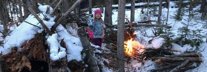 A young child smiling by a winter camp fire.