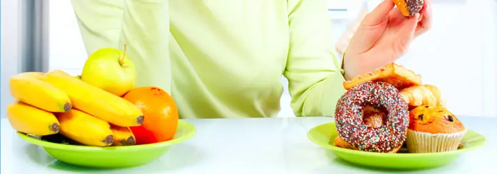 A person sitting in front of two plates of food. One has fruit and the other dessert.