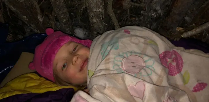 A young girl laying in a blanket and winter hat.