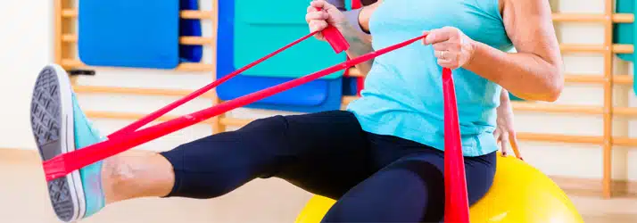 A physiotherapy patient sitting on an exercise ball and using resistance bands